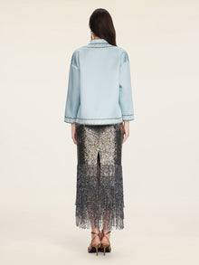 A woman stands with her back to the camera, wearing the Social Queen Floral Embroidered Beaded Jacket and a silver sequin fringe skirt, styled with gold heeled sandals.