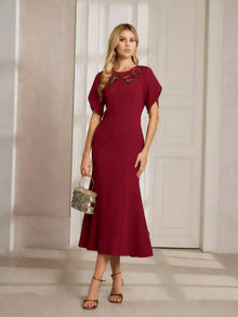 A woman indoors wears the Social Queen Floral Embroidered Beaded Mermaid Dress—calf-length, burgundy with 3D floral details—paired with strappy heels and a metallic handbag.