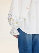 A person wears the Social Queen Floral Embroidered Cotton Blouse, featuring hand-embroidered floral and bow sleeve details, paired with blue jeans.
