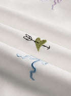Close-up of the Floral Embroidered Cotton Blouse by Social Queen in white, showcasing a green heart with an arrow and light blue and purple abstract lines.