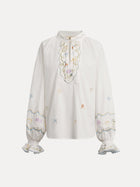 The Social Queen Floral Embroidered Cotton Blouse features a white long sleeve design with pastel embroidery, ruffled cuffs, and a tie-neck detail.