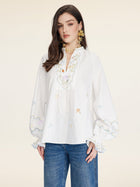 A woman wears the Social Queen Floral Embroidered Cotton Blouse with a relaxed fit and tie neckline, paired with blue jeans, standing against a plain light background.