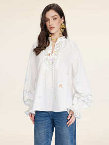 A woman wears the Social Queen Floral Embroidered Cotton Blouse with a relaxed fit and tie neckline, paired with blue jeans, standing against a plain light background.