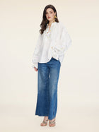 A woman stands against a plain background wearing the Social Queen Floral Embroidered Cotton Blouse, blue wide-leg jeans, and open-toe sandals.