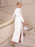 A woman in Social Queen’s Floral Embroidered Crystal Dress with a side slit and floral details, holding a silver handbag, ascends an elegant staircase—an ideal look for any sophisticated evening event.