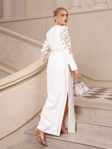 A woman in Social Queen’s Floral Embroidered Crystal Dress with a side slit and floral details, holding a silver handbag, ascends an elegant staircase—an ideal look for any sophisticated evening event.