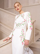 A woman wears the Social Queen Floral Embroidered Crystal Dress, featuring pink and green floral details, paired with a silver handbag and statement earrings—an elegant choice for evening occasions.