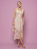 A woman stands against a pink background in the Social Queen Floral Embroidered Cutout Lace Dress, accessorized with a small handbag and open-toe sandals for an ideal semi-formal look.