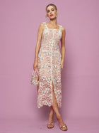 A woman stands against a pink background in the Social Queen Floral Embroidered Cutout Lace Dress, accessorized with a small handbag and open-toe sandals for an ideal semi-formal look.