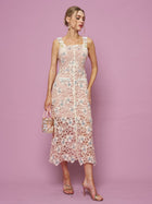 A woman stands elegantly against a pink background in the Social Queen Floral Embroidered Cutout Lace Dress, paired with a matching handbag and heeled sandals—an ideal choice for any semi-formal occasion.