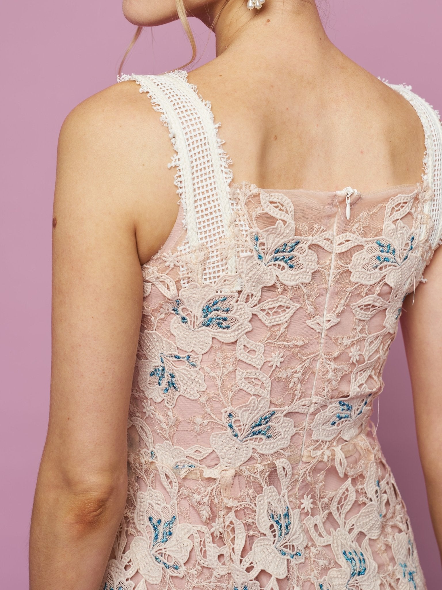 A person wearing the Social Queen Floral Embroidered Cutout Lace Dress—sleeveless, pink, with blue floral embroidery—stands against a light purple background.