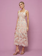 A woman poses against a pink background in the Social Queen Floral Embroidered Cutout Lace Dress—a sleeveless, knee-length, pale pink semi-formal dress with delicate floral embroidery—paired with strappy high-heeled sandals.