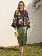 A woman in sunglasses and the Social Queen Floral Embroidered Puff Sleeve Jacket stands on grass by a white wall, styled with a green sequin skirt, heeled sandals, and a small box handbag.