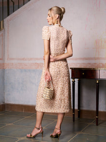 A woman in the Social Queen Floral Embroidered Lace Dress and heels stands indoors, facing away and holding a beaded handbag—an elegant choice for a wedding guest outfit.