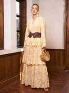 Indoors, a woman models the Social Queen Floral Embroidered Lace Layered Skirt, styled with a dark belt and wooden handbag near large windows—an elegant wedding guest look.