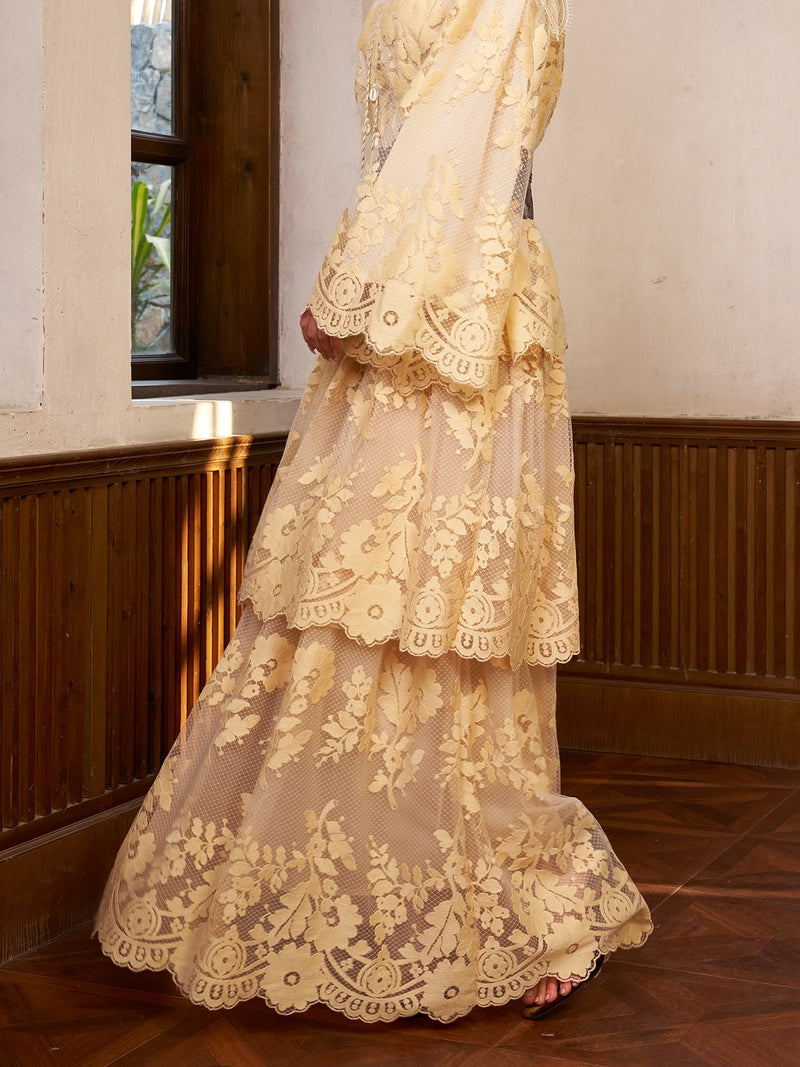 A person stands indoors by a wooden wall and window, wearing the Social Queen Floral Embroidered Lace Layered Skirt—a cream-colored, high-waist A-line skirt with 3D floral lace embroidery.