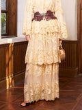 A person wears the Social Queen Floral Embroidered Lace Layered Skirt with a wide brown belt and holds a small wooden bag, standing indoors on a wooden floor—an ideal look for a wedding guest.