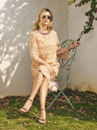A woman in a Social Queen Floral Embroidered Lace Midi Skirt and sunglasses sits on a metal chair in a garden, holding a small purse with flowers scattered around her.