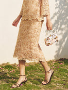 A woman walks outdoors on grass in the Social Queen Floral Embroidered Lace Midi Skirt and strappy sandals, carrying a small floral handbag.