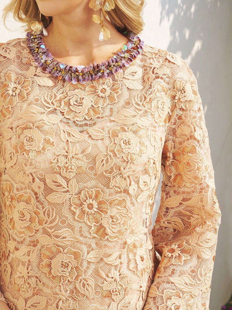 A person wearing the Social Queen Floral Embroidered Lace Top with Beaded Details, accessorized with gold drop earrings and a purple beaded necklace, stands in sunlight.
