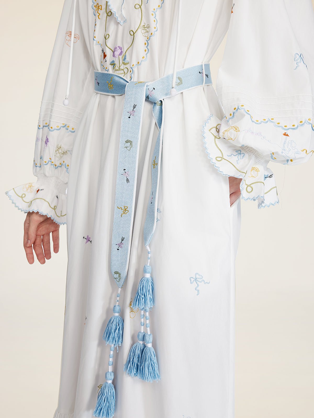A person wears the Social Queen Floral Embroidered Lantern Sleeve Dress, featuring hand-embroidered floral motifs and a light blue tasseled belt, capturing summer sophistication.