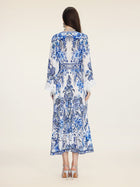 A woman stands facing away in the Social Queen Floral Embroidered Lantern Sleeve Dress, featuring blue patterns, lace cuffs, and heeled sandals, set against a plain light background.