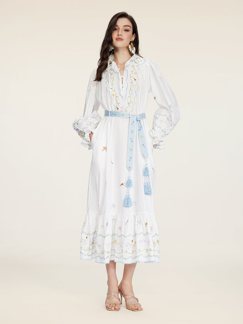 A woman wears the Social Queen Floral Embroidered Lantern Sleeve Dress with a blue tassel belt and beige sandals, standing against a plain light background—an ideal choice for summer sophistication.