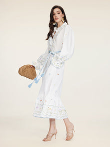 Woman in side profile wears the Social Queen Floral Embroidered Lantern Sleeve Dress with a blue belt, paired with a woven bag, beige heels, and statement earrings for a chic summer look.