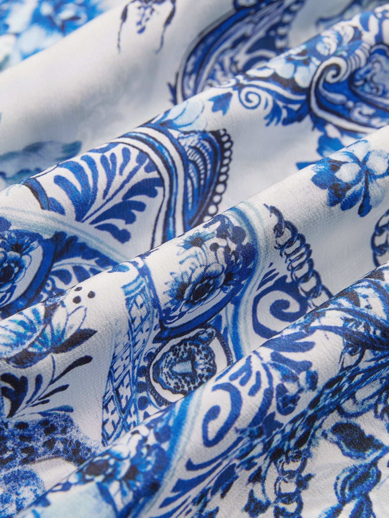 Close-up of fabric from the Social Queen Floral Embroidered Lantern Sleeve Dress, featuring blue and white floral and paisley patterns with intricate designs and elegant folds.