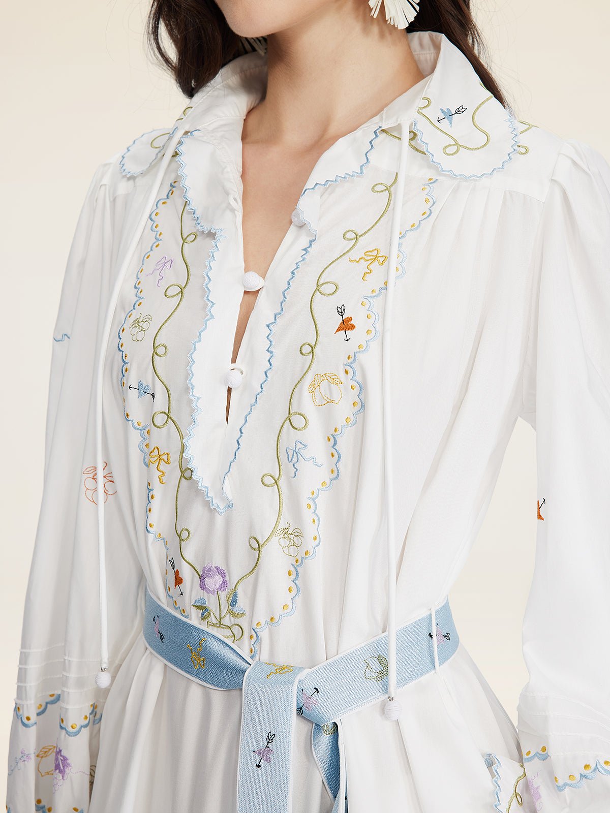 A woman wears the Social Queen Floral Embroidered Lantern Sleeve Dress, featuring scalloped edges, hand-embroidered floral motifs, and a light blue belt—ideal as a vacation-ready look. Shown from shoulders to waist.