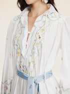 A woman wears the Social Queen Floral Embroidered Lantern Sleeve Dress, featuring scalloped edges, hand-embroidered floral motifs, and a light blue belt—ideal as a vacation-ready look. Shown from shoulders to waist.