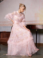 A woman in the Social Queen Floral Embroidered Layered Tulle Dress sits on a brown vintage-style couch with her hand on the skirt, next to a wooden table and against a textured wall.