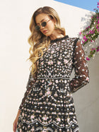 A woman in sunglasses wears the Social Queen Floral Embroidered Mesh Dress, standing outdoors by a white wall and blooming pink flowers.