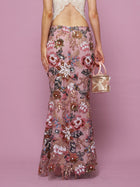 Against a pink background, a person wears the Social Queen Floral Embroidered Sequin Mermaid Skirt with a backless lace top and holds a small pink handbag.
