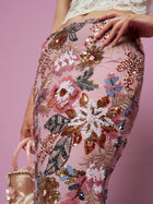 A person wears the Social Queen Floral Embroidered Sequin Mermaid Skirt and holds a small beaded handbag against a pink background.