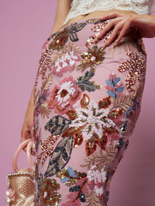 A person wears the Social Queen Floral Embroidered Sequin Mermaid Skirt and holds a small beaded handbag against a pink background.