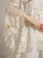 A person wears the Social Queen Floral Embroidered Sheer Overlay Top, featuring delicate lace, beadwork on sleeves and bodice, and an elegant cape silhouette.