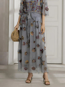 A person in a Social Queen Floral Embroidered Silk A-Line Skirt stands by a white door, pairing the skirt with open-toe heels and a small straw handbag.
