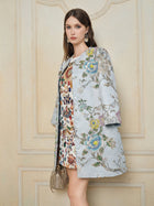 Indoors, a woman wears the Social Queen Floral Embroidered Silk Jacquard Jacket over a colorful dress, accessorized with a small textured handbag and large earrings.