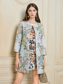 A woman indoors wears the Social Queen Floral Embroidered Silk Jacquard Jacket over a colorful dress, accessorized with long earrings, straight hair, and a small woven handbag.