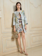 Indoors, a woman wears the Social Queen Floral Embroidered Silk Jacquard Jacket over a colorful dress, paired with high-heeled sandals and a small handbag.