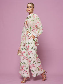A woman poses against a pink background wearing Social Queen's Floral Embroidered Textured Wide-Leg Pants, paired with gold heels and a small handbag.