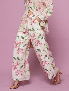 A model wears Social Queen's Floral Embroidered Textured Wide-Leg Pants with gold heels, walking against a pink background.