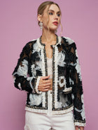 Against a pink background, a woman wears the Social Queen Floral Embroidered Tulle Beaded Jacket over a white top and pants, styled with statement earrings.