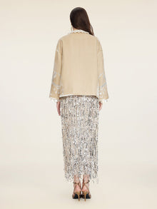 A woman faces away wearing Social Queen's Floral Embroidered Velvet Jacket and a long silver fringe skirt with black strappy heels, set against a plain light background.