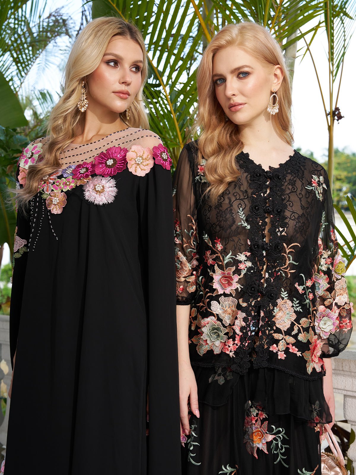 Two women stand outdoors among green palms, each in a Social Queen Floral Embroidery 100% Mulberry Silk Tulle Blouse paired with black dresses featuring sheer details.