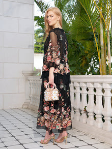 A woman stands on a tiled balcony, holding a white handbag and wearing the Social Queen Floral Embroidery 100% Mulberry Silk Tulle Blouse, with greenery and white stone railings in the background.