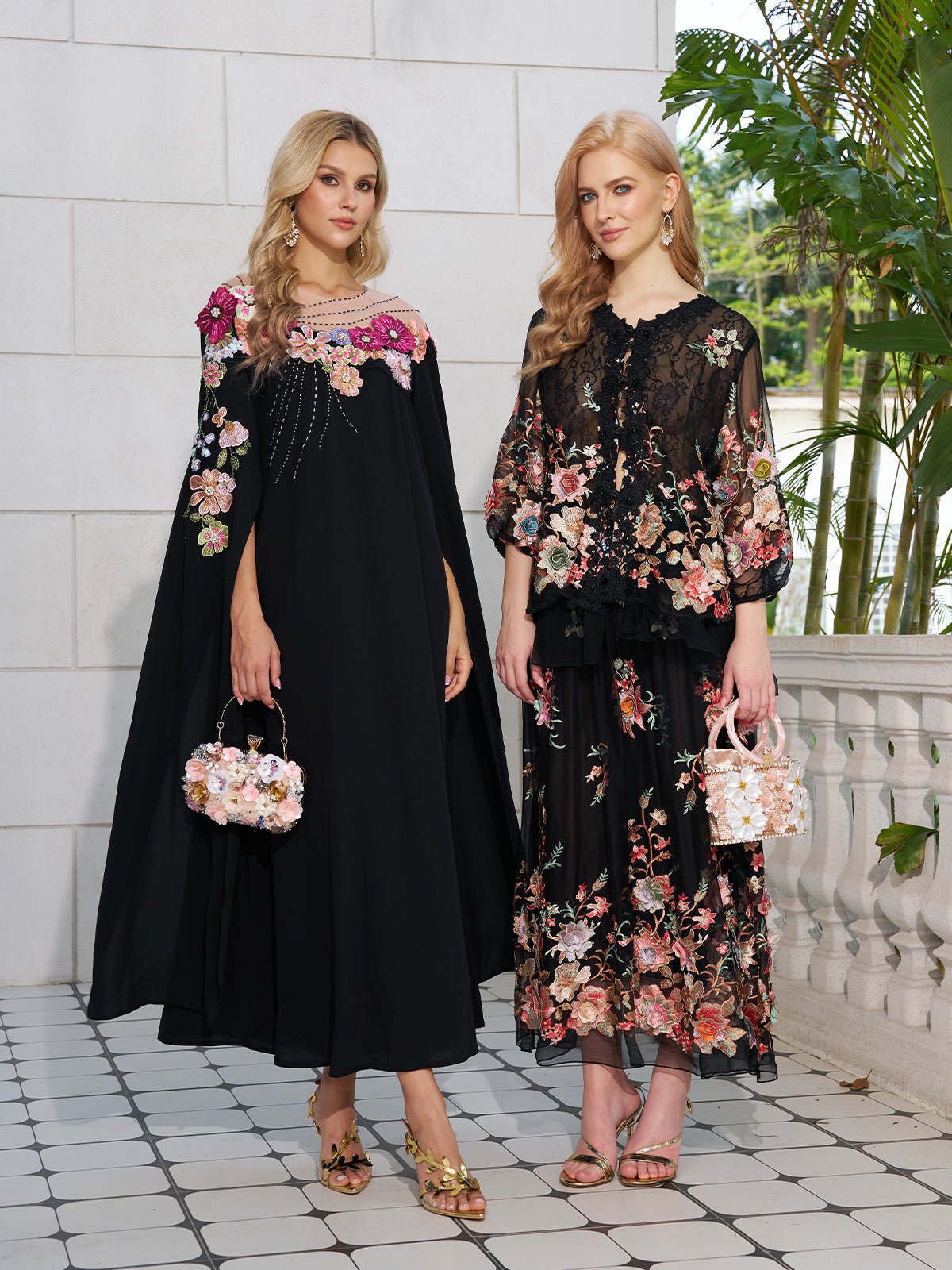 Two women wear Social Queen’s Floral Embroidery 100% Mulberry Silk Tulle Skirts, paired with floral handbags, standing against a backdrop of a light stone wall and greenery.