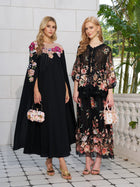 Two women wear Social Queen’s Floral Embroidery 100% Mulberry Silk Tulle Skirts, paired with floral handbags, standing against a backdrop of a light stone wall and greenery.