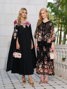 Two women wear Social Queen’s Floral Embroidery 100% Mulberry Silk Tulle Skirts, paired with floral handbags, standing against a backdrop of a light stone wall and greenery.